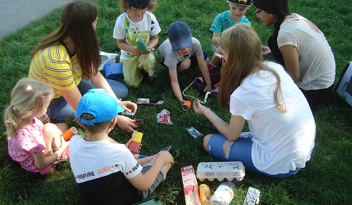 Kinder sitzen im Kreis auf dem Rasen und üben Abfalltrennung